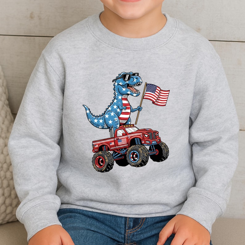 A child wearing a gray sweatshirt with a cartoon image of a dinosaur riding a red truck with American flags on the hood.