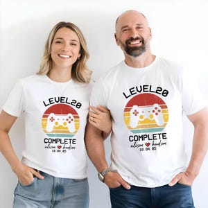 May include: Two white t-shirts with a retro video game controller graphic and the text "Level 20 Complete" with a heart and names. The text below the graphic says "Alison Hudson 10.04.85".