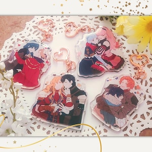 May include: Four colourful acrylic keychains featuring anime couples. Each keychain has a heart-shaped charm attached to a gold-coloured chain.
