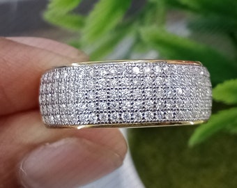 May include: A gold band ring with a wide band covered in small, clear cubic zirconia stones.