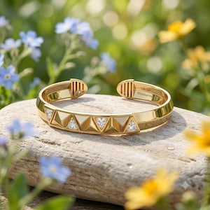 May include: A gold-tone cuff bracelet featuring a geometric pattern of alternating smooth triangular facets and triangular cut-out sections set with small clear stones. The interior is engraved with the text 14k GP Moissanite.