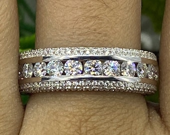 May include: A silver band ring with a row of large round diamonds set in a channel setting. The ring has two rows of smaller diamonds on either side of the larger diamonds.