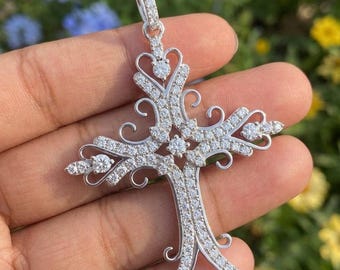 May include: A silver-toned cross pendant featuring intricate filigree scrollwork and numerous small, clear, sparkling stones embedded throughout the metal frame, including a larger round stone at the center and at each of the four ends.