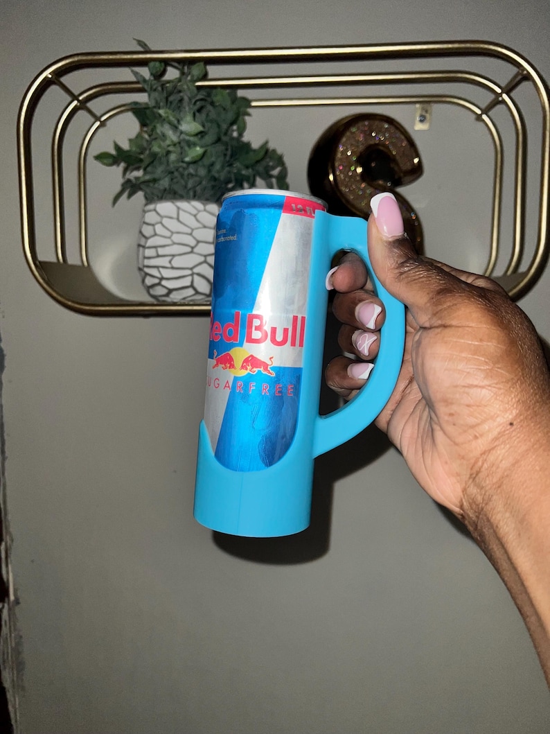 May include: A blue can holder with a handle. The can holder is holding a blue and red Red Bull Sugarfree can.