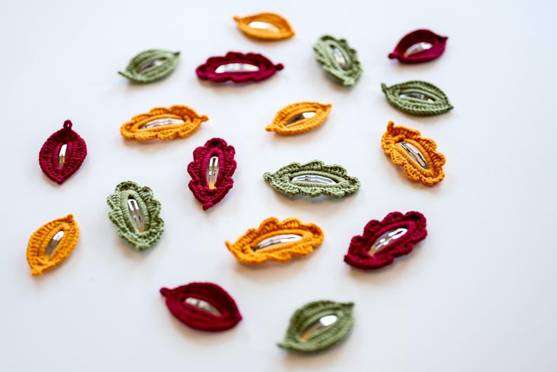 May include: Assortment of crocheted leaf-shaped hair clips in green, red, and yellow.