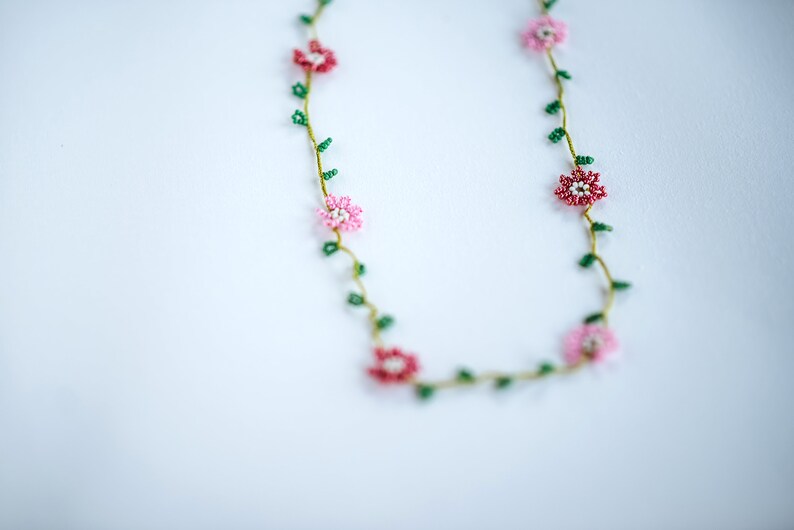 Pu&ograve; includere: Una delicata collana di perline con fiori rosa e rossi e foglie verdi. La collana &egrave; realizzata con piccole perline ed &egrave; infilata su un filo sottile.