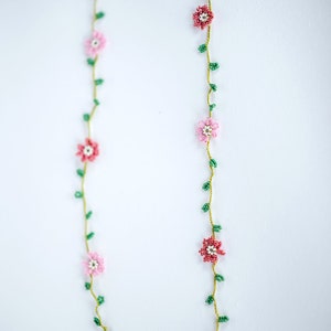 Pu&ograve; includere: Una catena per occhiali in perle con fiori rosa e rossi e foglie verdi.