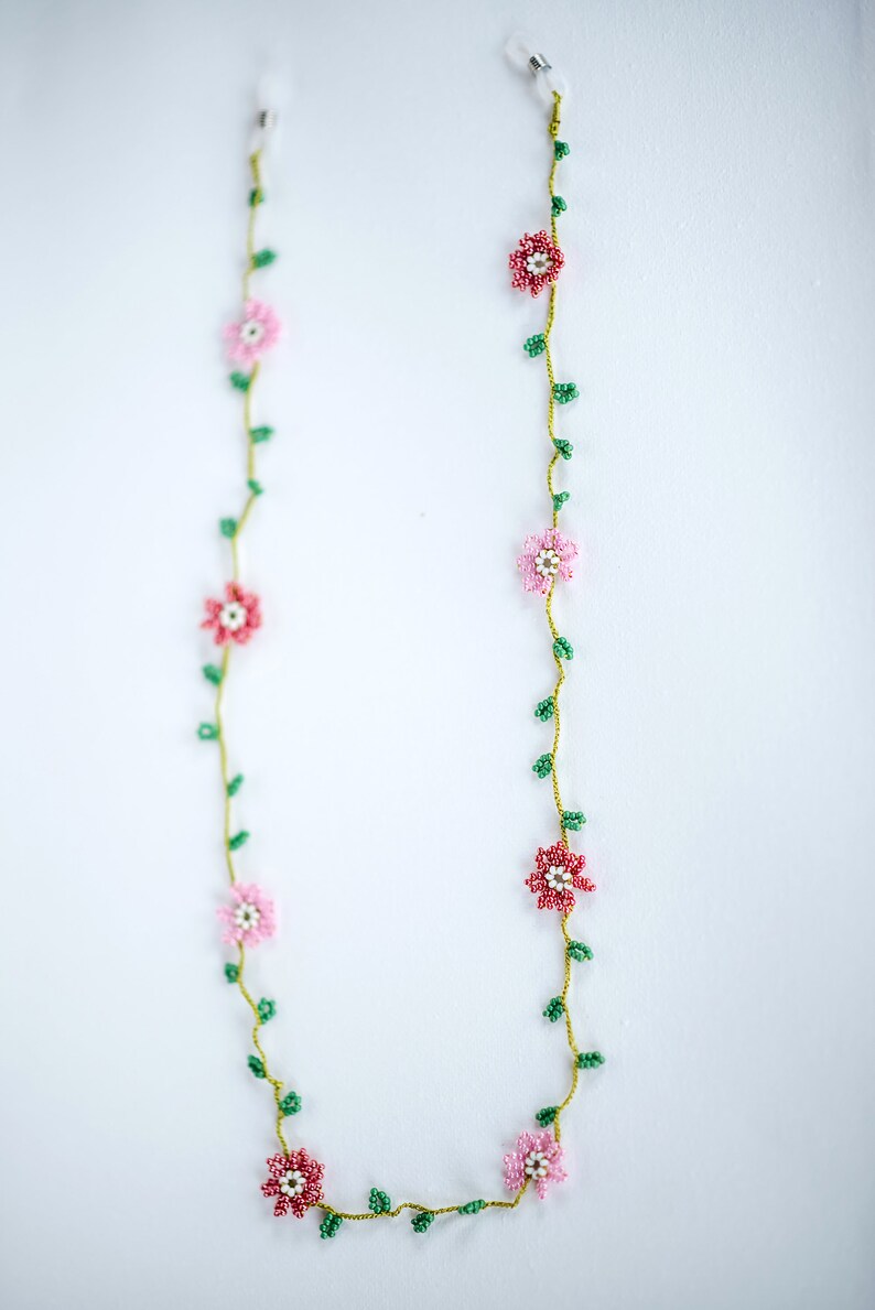 Pu&ograve; includere: Una catena per occhiali in perle con fiori rosa e rossi e foglie verdi.