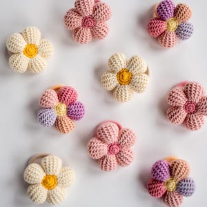 K&ouml;nnte beinhalten: Ein Set mit zehn bunten geh&auml;kelten Blumenhaargummis. Die Haargummis sind in verschiedenen Farben gehalten, darunter Rosa, Gelb und Lila. Jedes Haargummi hat ein Blumendesign mit einem Knopf in der Mitte.
