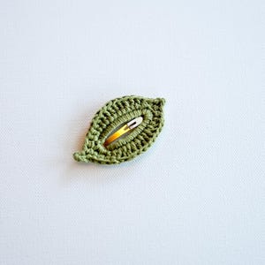 May include: A green crocheted leaf-shaped hair clip with a gold metal bar.