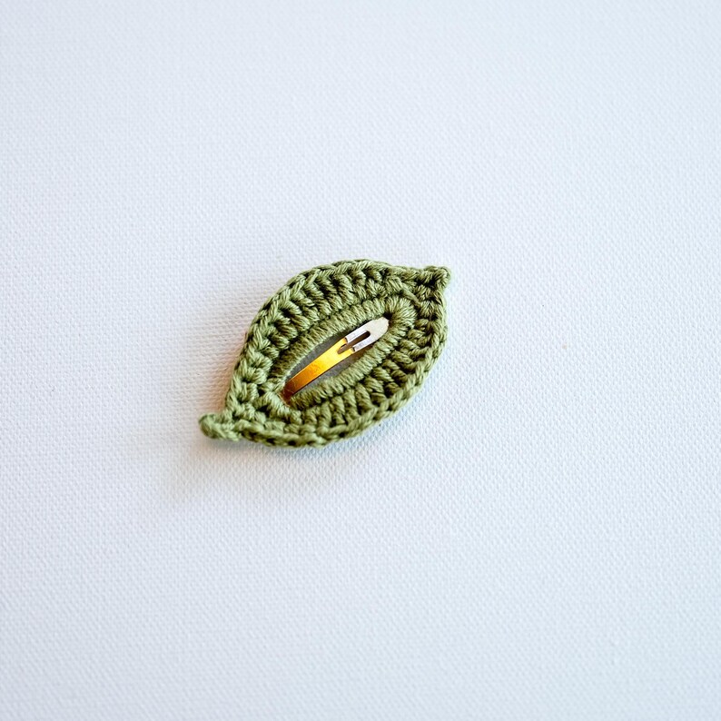May include: A green crocheted leaf-shaped hair clip with a gold metal bar.