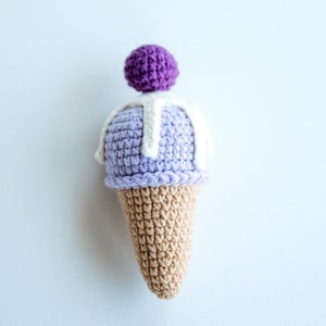 May include: A crocheted ice cream cone toy with a purple and white ice cream scoop and a white swirl on top.