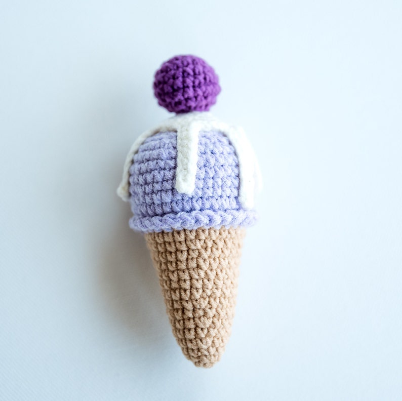 May include: A crocheted ice cream cone toy with a purple and white ice cream scoop and a white swirl on top.