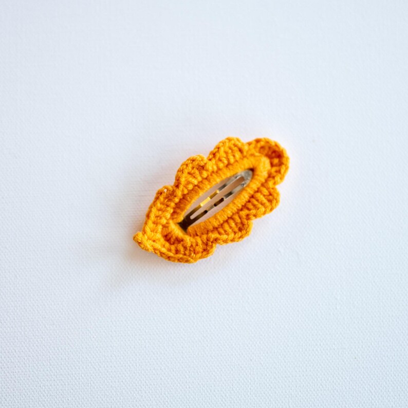 May include: A crocheted orange leaf-shaped hair clip with a metal clasp.