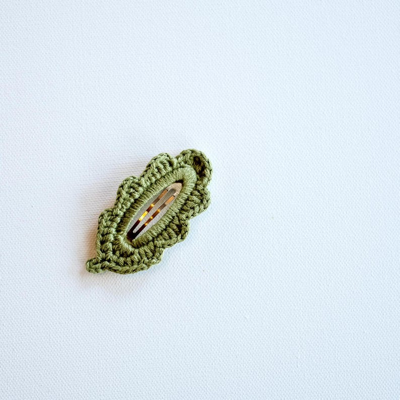 May include: A green crocheted leaf-shaped hair clip with a silver metal clasp.