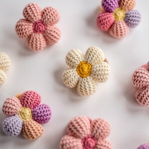 K&ouml;nnte beinhalten: Ein Set mit sechs geh&auml;kelten Blumenhaargummis in verschiedenen Farben, darunter Rosa, Wei&szlig; und Lila. Die Blumen haben ein schlichtes, g&auml;nsebl&uuml;mchenartiges Design mit einem Knopf in der Mitte.
