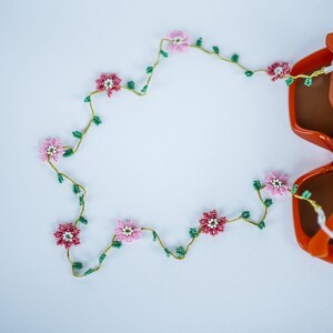 Pu&ograve; includere: Un paio di occhiali da sole arancioni con una catena di fiori perlati. La catena ha fiori rosa e bianchi con foglie verdi.