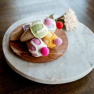 May include: A set of five crocheted ice cream cones in various colors, including pink, yellow, green, and white, displayed on a wooden platter atop a marble surface.