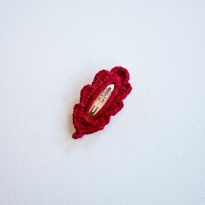 May include: A burgundy crocheted leaf-shaped hair clip with a gold metal clasp.