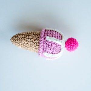 May include: A crocheted ice cream cone toy with pink and white ice cream and a pink cherry on top.