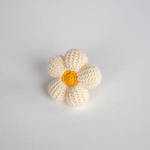 K&ouml;nnte beinhalten: Eine geh&auml;kelte wei&szlig;e G&auml;nsebl&uuml;mchen-Blume mit gelber Mitte.