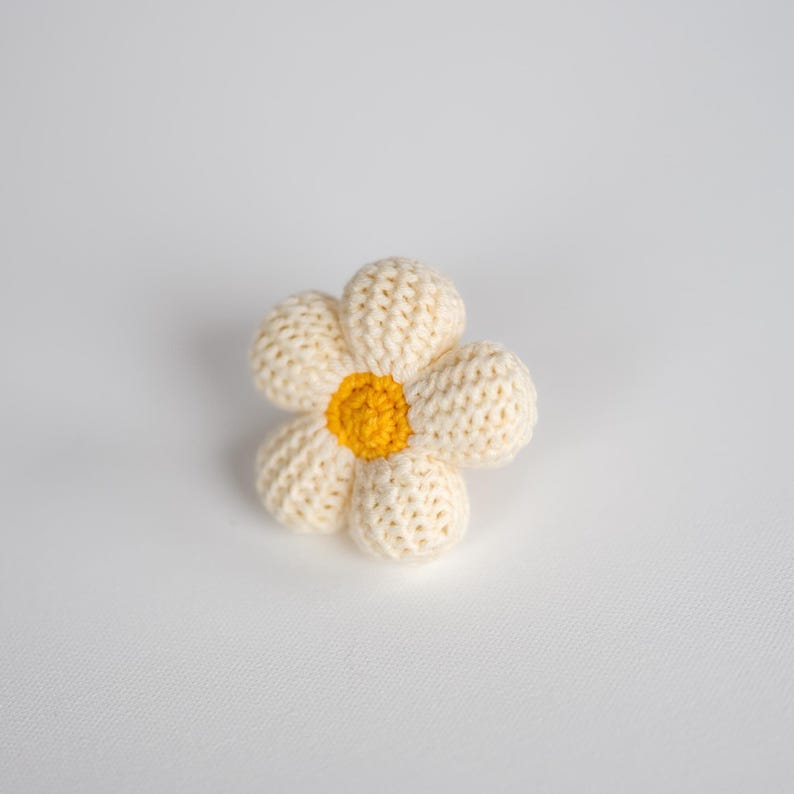 K&ouml;nnte beinhalten: Eine geh&auml;kelte wei&szlig;e G&auml;nsebl&uuml;mchen-Blume mit gelber Mitte.