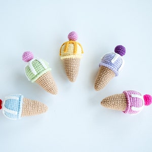 May include: Five crocheted ice cream cones in different colors, including pink, purple, green, yellow, and blue. Each cone has a white crocheted swirl on top.