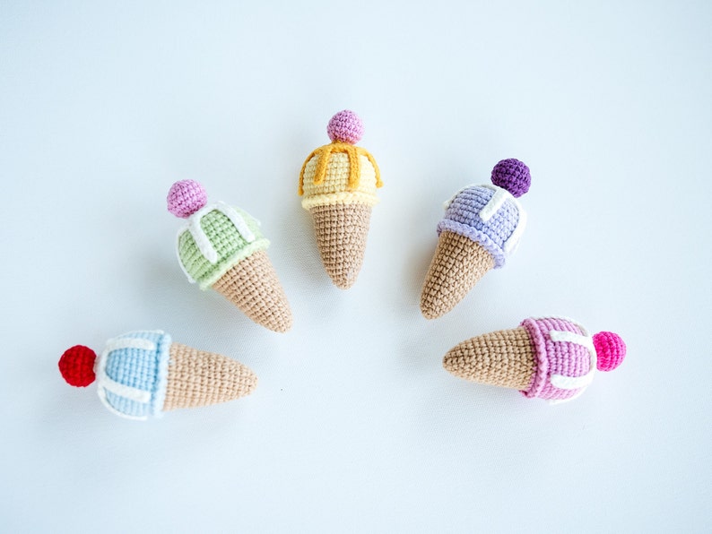 May include: Five crocheted ice cream cones in different colors, including pink, purple, green, yellow, and blue. Each cone has a white crocheted swirl on top.