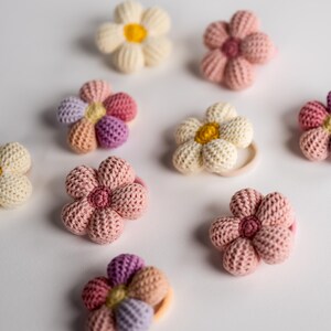 K&ouml;nnte beinhalten: Ein Set mit zehn geh&auml;kelten Blumenhaargummis in verschiedenen Rosat&ouml;nen, Wei&szlig; und Gelb. Die Haargummis sind aus weichem, strukturiertem Garn gefertigt und haben ein schlichtes Blumendesign.