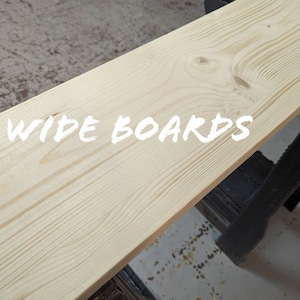 May include: A close-up of a wide, light wood board. The board is smooth and has a natural grain pattern. The text "WIDE BOARDS" is written in white across the board.