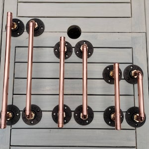 May include: Six copper pipe door handles with black flanges. The handles are different lengths and have a polished finish.