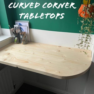 May include: A light wood curved corner tabletop with a white and green wall behind it. The text "CURVED CORNER TABLETOPS" is written in white on the green wall.