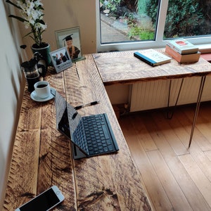 K&ouml;nnte beinhalten: Ein rustikaler L-f&ouml;rmiger Schreibtisch aus Holz mit einem Laptop, einem Telefon und einer Kaffeetasse auf der Oberfl&auml;che. Der Schreibtisch hat eine nat&uuml;rliche Holzoptik und wird von Haarnadelbeinen getragen.