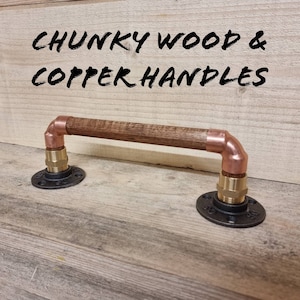 Puede incluir: Una manija de puerta de madera con extremos de tubería de cobre y bridas de metal negro. La manija está etiquetada como "CHUNKY WOOD & COPPER HANDLES".