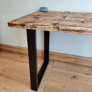 May include: A rustic wooden table with a black metal frame. The table has a distressed finish and is supported by two square legs.