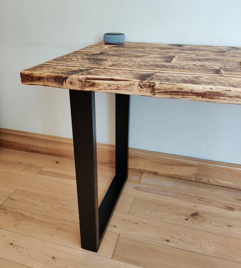 May include: A rustic wooden table with a black metal frame. The table has a distressed finish and is supported by two square legs.
