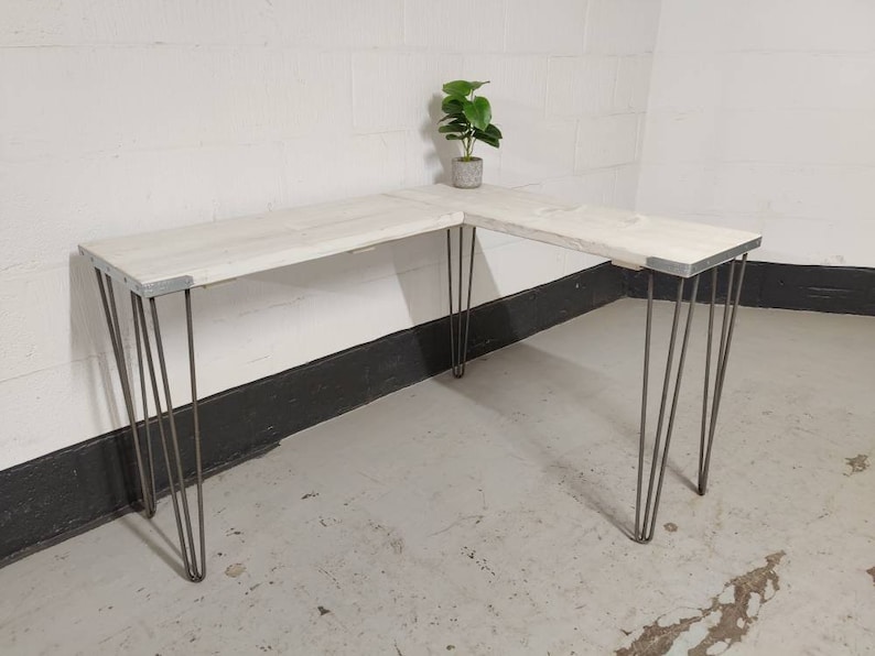 K&ouml;nnte beinhalten: Wei&szlig;er Ecktisch mit Haarnadelbeinen. Der Tisch ist aus recyceltem Holz und hat einen rustikalen Look.