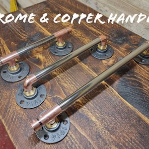 May include: Three industrial style cabinet handles with copper and chrome finishes. The handles are made of metal pipe with black flanges and copper caps. The flanges are stamped with the number "1914".