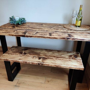 May include: A rustic wooden table and bench set with black metal legs. The table top and bench seat are made of reclaimed wood with a natural finish.