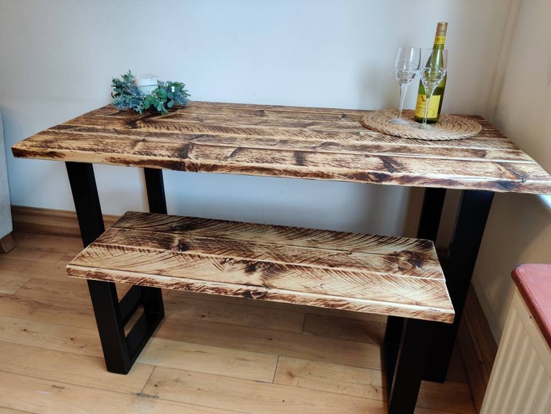 May include: A rustic wooden table and bench set with black metal legs. The table top and bench seat are made of reclaimed wood with a natural finish.