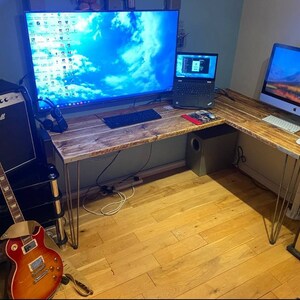 K&ouml;nnte beinhalten: Ein Ecktisch mit einer Holzplatte und Metall-Haarnadelbeinen. Auf dem Tisch stehen ein Computermonitor, ein Laptop und eine Gitarre. Im Hintergrund befinden sich au&szlig;erdem ein Lautsprecher und ein Aquarium.