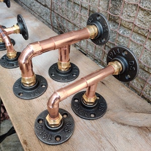 May include: Four copper pipe fittings with black iron flanges. Each flange has a number and the letters "DS" printed on it. The fittings are connected together in a line.