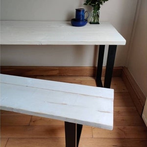 May include: White wooden bench with black metal legs. The bench is sitting on a wooden floor.