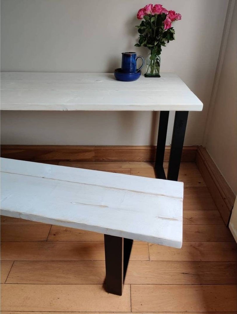 May include: White wooden bench with black metal legs. The bench is sitting on a wooden floor.
