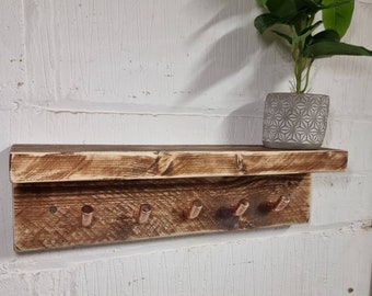 Könnte beinhalten: Ein rustikales Holzregal mit fünf Kupferhaken, perfekt zum Aufhängen von Schlüsseln, Schmuck oder anderen kleinen Gegenständen. Das Regal hat eine abgenutzte Oberfläche und ist an einer weißen Wand montiert.