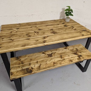 May include: A rustic wooden table and bench set with a black metal frame. The table and bench have a distressed wood finish and are perfect for a farmhouse or industrial style dining area.