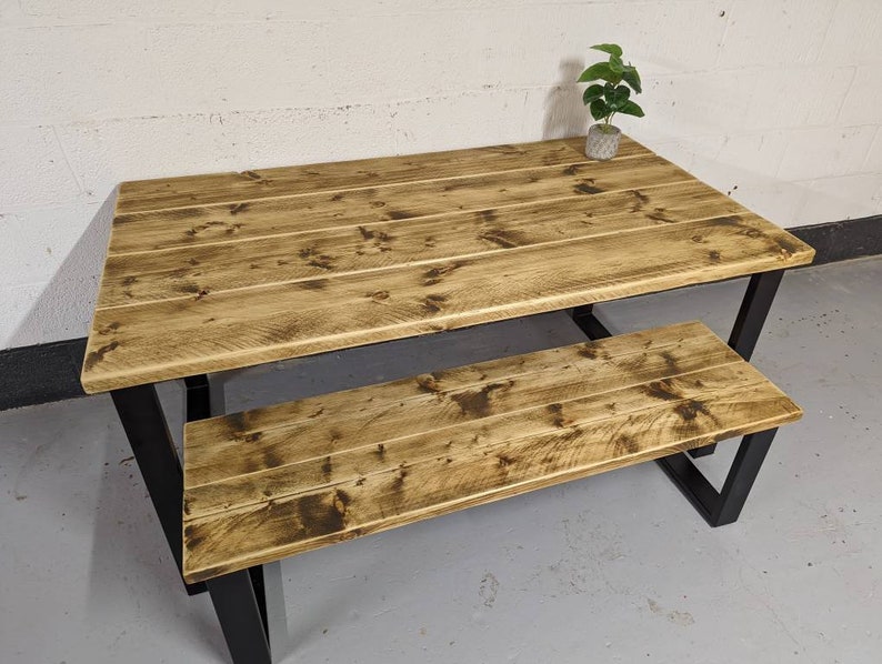 May include: A rustic wooden table and bench set with a black metal frame. The table and bench have a distressed wood finish and are perfect for a farmhouse or industrial style dining area.