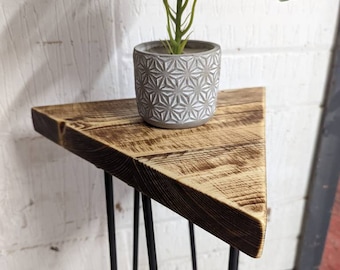 Könnte beinhalten: Ein dreieckiger Holztisch mit schwarzen Haarnadelbeinen. Eine kleine Topfpflanze mit grünen Blättern steht auf der Tischplatte.