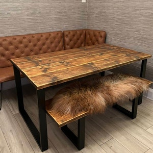 May include: A rustic wooden dining table with black metal legs and a matching bench. The table top is made of reclaimed wood with a distressed finish. The bench has a sheepskin cushion.