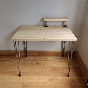 May include: A wooden desk with a natural finish and hairpin legs. The desk has a small shelf above the main surface, supported by copper pipes.